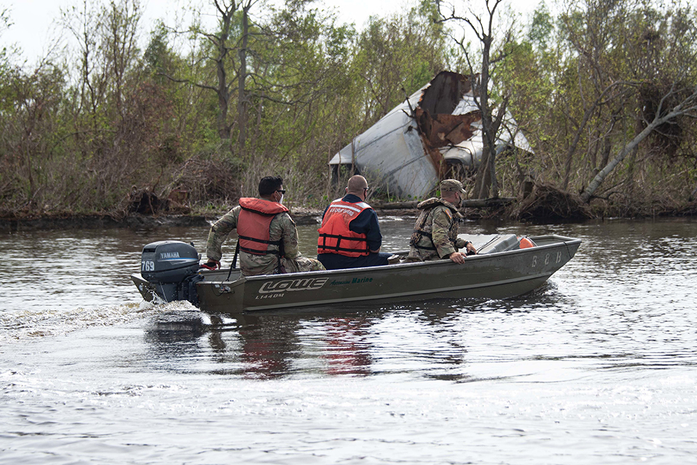 Louisiana National Guard Spc. Micheal Cotton, left, operates a National Guard boat as Coast Guard Lt. David Schneider, center, inspects hazards to navigation, and National Guard 2nd Lt. Stuart Coles maintains a sharp lookout for debris on the Houma Navigation Canal in Houma, Louisiana, Sept. 13, 2021.