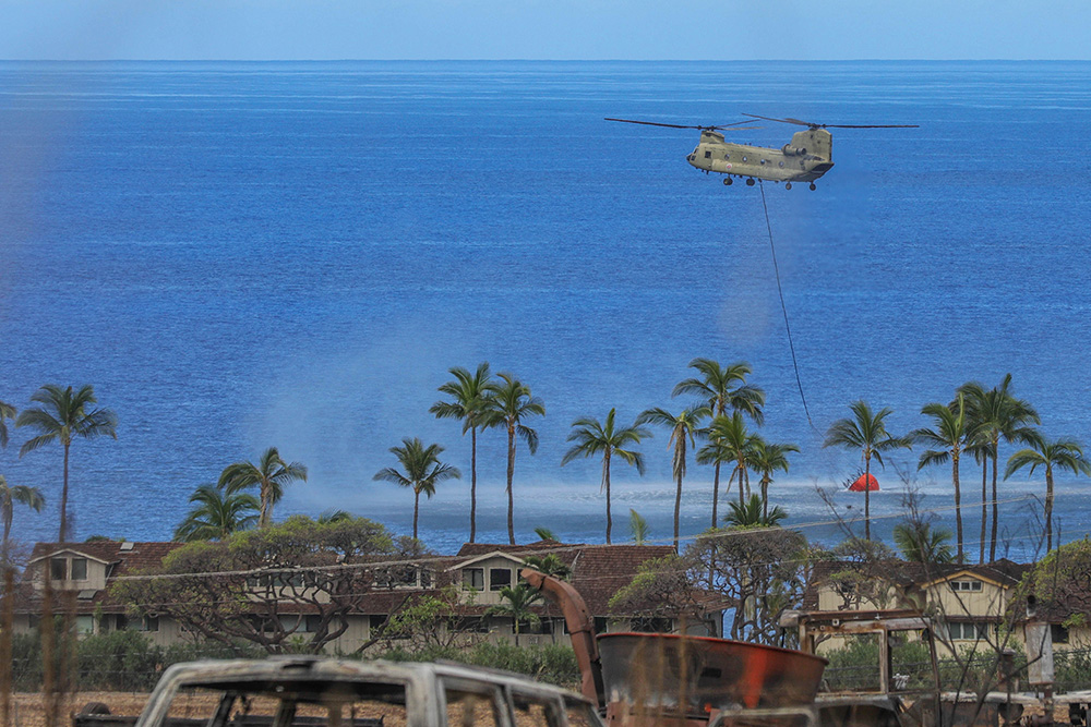 An Army CH-47 Chinook fills a bucket with water to drop around the perimeter of an area impacted by the wildfires in the town of Lahaina on Maui, Hawaii, Aug. 16, 2023.