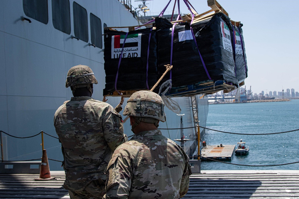 U.S. Army soldiers with the 7th Transportation Brigade (Expeditionary) use a rope to stabilize humanitarian aid while it is lifted by a crane aboard the MV Roy P. Benavidez at the Port of Ashdod, Israel. © Army Staff Sgt. Malcolm Cohens-Ashley
