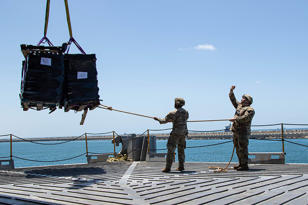 Soldiers assigned to the Army’s 7th Transportation Brigade (Expeditionary) use a rope to stabilize humanitarian aid supplies while it is lifted by a crane aboard the MV Roy P. Benavidez to support the Joint Logistics Over-The-Shore operation, in the Port of Ashdod, Israel, May 13, 2024. © Army Staff Sgt. Malcolm Cohens-Ashley