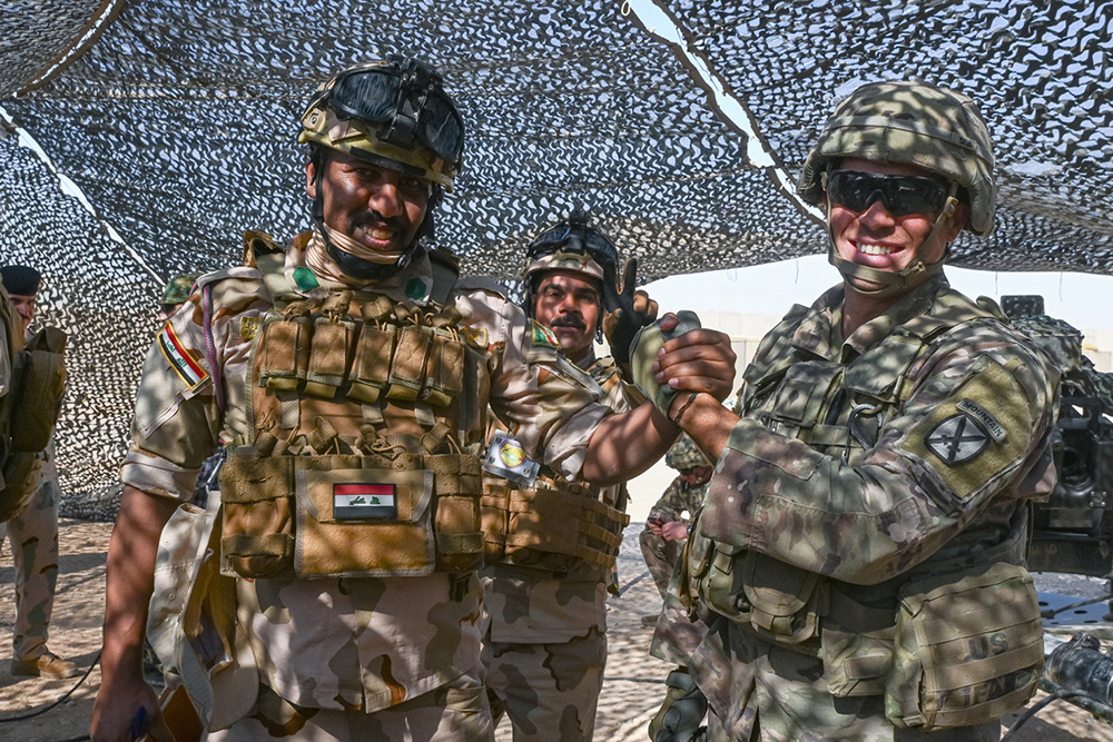 A soldier assigned to the Army’s 10th Mountain Division, poses for a photo with two Iraqi army artillery soldiers during a joint artillery training exercise at Al Asad Air Base, Iraq, on Oct 26, 2023. © Army 2nd Lt. Daphney Black