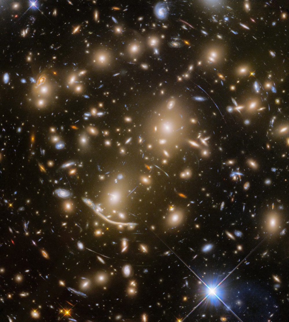 Abell 370, a galaxy cluster located nearly 4 billion light-years away from Earth features several arcs of light, including the "Dragon Arc" (lower left of center). These arcs are caused by gravitational lensing: Light from distant galaxies far behind the massive galaxy cluster coming toward Earth is bent around Abell 370 by its massive gravity, resulting in contorted images. © NASA